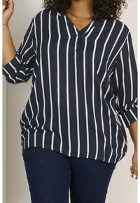Blouse à rayures bleu marine avec des rayures blanches verticales, présentant un décolleté en V et des manches 3/4, fabriquée dans un tissu lisse.