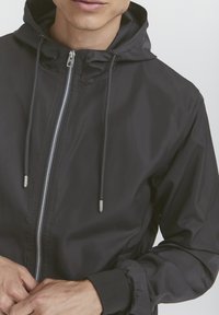Sort letvægts hættetrøje med frontlynlås, snore, elastiske manchetter og en glat tekstur. Klassisk design uden synlige mønstre.