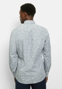 Hemd mit Knopfleiste in Hellblau mit einem Blumenmuster in Marineblau und Grün. Lange Ärmel, klassischer Kragen und abgerundeter Saum. Weiche Stoffstruktur.