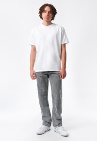 T-shirt bianco in cotone abbinato a pantaloni in denim grigi. I pantaloni presentano una trama leggermente vissuta. Completato con sneakers bianche.
