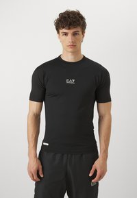 Svart kortermet treningst-skjorte laget av smooth, elastisk stoff med en liten hvit logo på brystet og en tettsittende design.