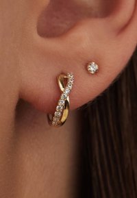 Créoles en or avec un design tordu, ornées de pierres précieuses transparentes sur un côté et d'une petite boucle d'oreille en stud ronde.