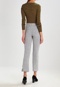 Svart och gulrandig långärmad topp ihop med ljusgrå stickade byxor med utsvängd nederdel och sidofickor, bärs med svarta klackskor.