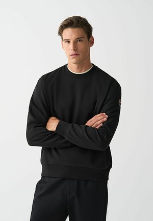 Zwarte sweatshirt met een geribde ronde hals en manchetten, voorzien van een klein logo patch op de mouw. Zacht, gestructureerd materiaal.