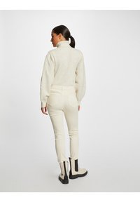 Suéter de punto crema con un cuello alto, combinado con pantalones blancos ajustados y botas negras hasta el tobillo con un panel lateral en contraste.