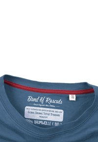 Blaue Baumwoll-T-Shirt mit rundem Hals und rotem Akzent. Das Etikett zeigt den Markennamen und Pflegeanweisungen und hebt die Verwendung von organischen Materialien hervor.