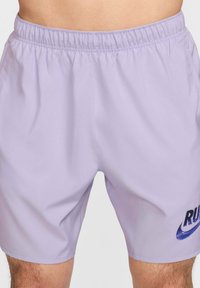 Pantalones cortos atléticos de color lila con cintura elástica, con un logo azul de Nike y el texto "RUN" en el lado izquierdo. Material suave y ligero.