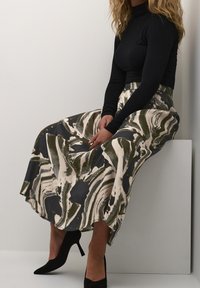 Haut à col roulé noir associé à une jupe mi-longue avec un motif abstrait tourbillon vert et crème. Des chaussures à talons hauts noires complètent la tenue.