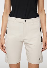 Beiga shorts med en slät textur, med svarta dragkedjefickor, knappstängning framtill och en logodetalj vid fållen.