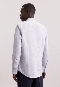 Camicia slim-fit di colore azzurro chiaro con un piccolo motivo floreale multicolore, dotata di colletto classico, maniche lunghe e polsini con bottone.