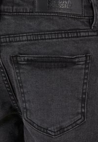 Svarte denimjeans har en synlig baklomme med utstikkende sømmer. Det finnes et lærmerke merket "Urban Classics Denim Factory".