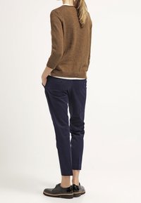 Maglione marrone a maglia testurizzata con maniche a tre quarti abbinato a pantaloni tapered blu e scarpe stringate in vernice nera.