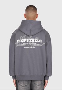 Grauer Kapuzenpullover mit Kordelzugkapuze, ausgestattet mit weißem Drucktext auf dem Rücken. Rippbündchen und Saum. Weicher Stoff mit lässigem Schnitt.