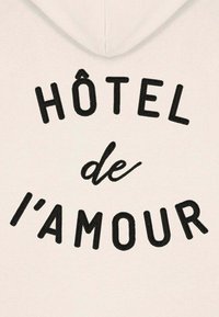 Felpa cappuccio bianca con testo ricamato nero che recita "HÔTEL de l'amour", dal design curvo e una texture morbida e liscia.
