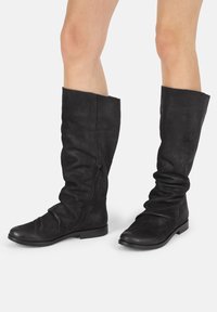 Black leather knee-high boots with a slouchy design, side zipper detail, round toe, and flat sole. Smooth texture with minimal accents.