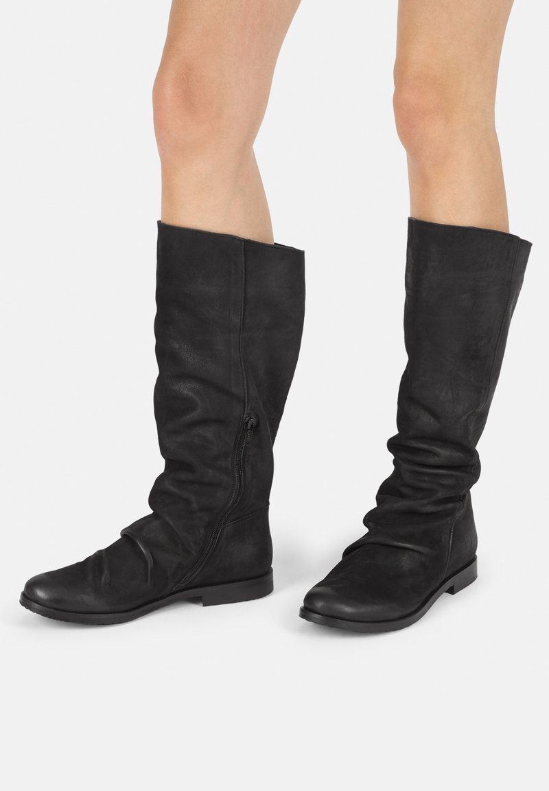 Black leather knee-high boots with a slouchy design, side zipper detail, round toe, and flat sole. Smooth texture with minimal accents.