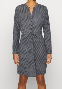 Robe bleue à motifs avec manches longues, fermeture à boutons et ceinture à la taille. Le tissu a une texture douce avec un motif floral subtil.