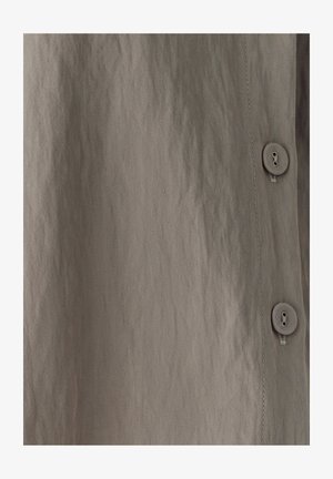 Buttoned shirt featuring a textured, light brown fabric with a subtle sheen. Smooth texture, vertical seams, and round buttons are visible.