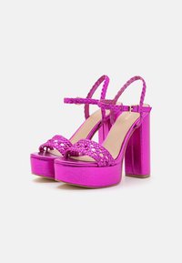 Sandalias de plataforma en fucsia con una correa trenzada, diseño de punta abierta y un tacón cuadrado grueso. Fabricadas con un material sintético brillante y una textura suave.