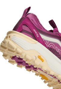 Крупен план на лилав туристически обувка Gore-Tex с бежова и лилава Vibram подметка и дръжки за дърпане на петата и езици.