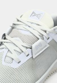 Light grey athletic shoe with textured mesh upper, white accents, visible laces, and a logo tag on the tongue in smooth material.