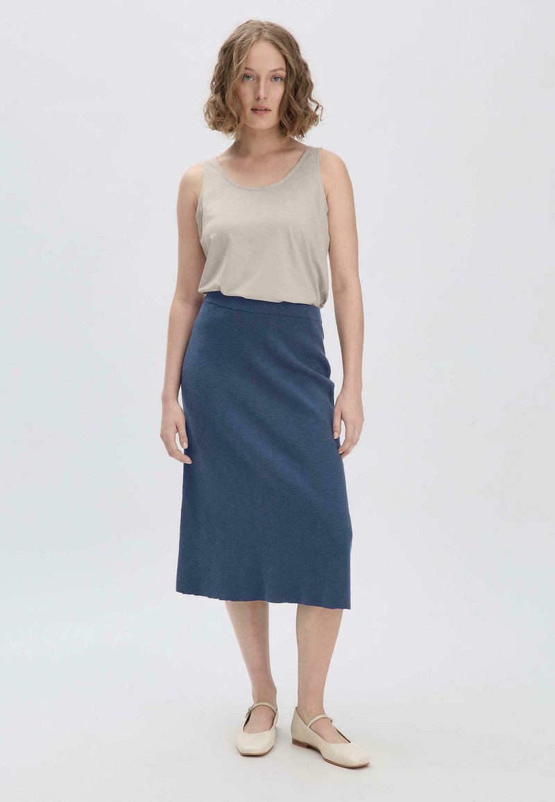 Beige ärmelloses Oberteil und dunkelblaue, knielange, taillierte Rock mit einer subtilen Textur. Minimalistisches Design mit flachen, hellfarbigen Schuhen.