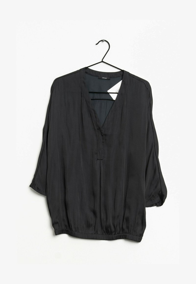 Blouse noire à manches longues avec col en V, coupe ample et ourlet élastique, suspendue à un cintre noir sur un fond blanc.