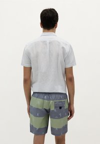 Chemise à col à manches courtes de couleur bleu clair avec de fines rayures blanches, associée à un short de bain vert et gris avec un motif de crâne.