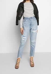 Ljusblå ripped jeans med fransade fållar, bärs med en svart läderjacka och en vit randig långärmad skjorta. Svarta sandaler med remmar.