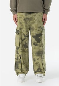 Pantalones cargo con un patrón de camuflaje, que presentan grandes bolsillos laterales, hechos de una tela texturizada y duradera en tonos de verde oliva.