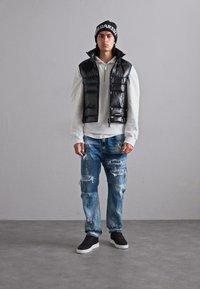 Vesta puffer neagră peste un hanorac alb, asortată cu blugi albaștri deteriorați și adidași negri. Accesoriile includ o căciulă neagră tricotată.