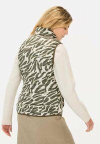 Groene en witte gestreepte puffer vest met hoge kraag, voorzien van horizontale stiksels en een getailleerd ontwerp, gedragen over een lichte trui.