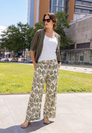 Lichtgewicht olijfgroene cardigan, wit tanktopje en wijde broek met een groen bladerenpatroon. Gecombineerd met beige slippers en een zonnebril.