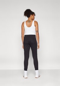 Sorte joggebukser med elastiske mansjetter og sidestriper, kombinert med en hvit tanktop. Glatt tekstur, atletisk design og avslappet passform.