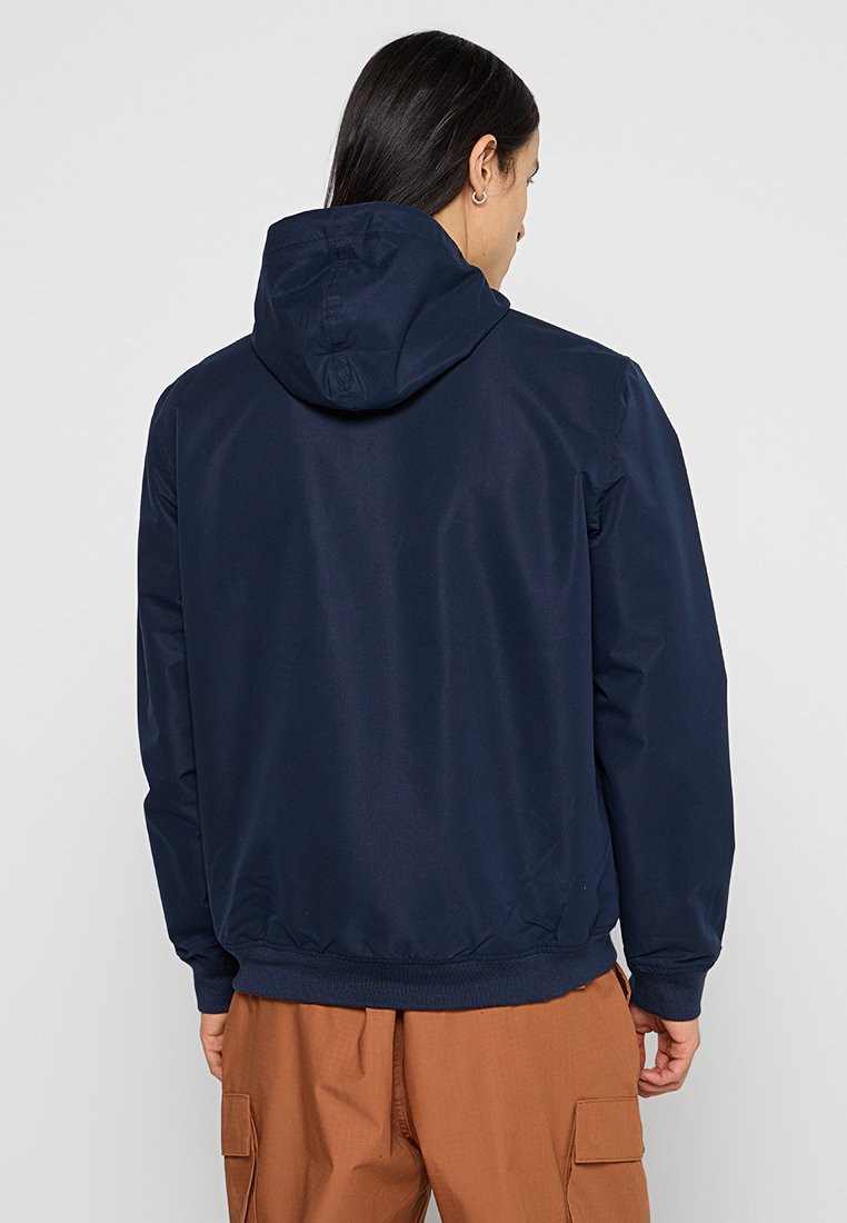 Granatowa kurtka z kapturem wykonana z gładkiego materiału, z elastycznym pasem i mankietami. Widok z tyłu pokazuje minimalne detale.