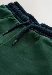 Green sweatpants with a navy ribbed waistband, featuring a drawstring and subtle fabric texture. Soft cotton blend for comfort.