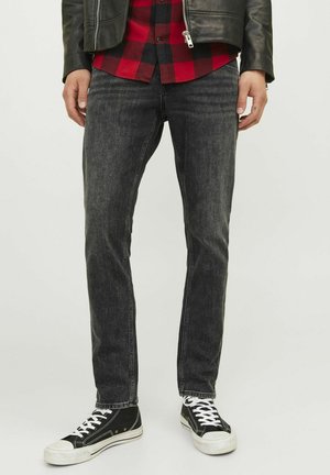 Jeans de denim negro con corte slim, que presentan una textura ligeramente desgastada y un corte recto, combinados con zapatillas altas negras.