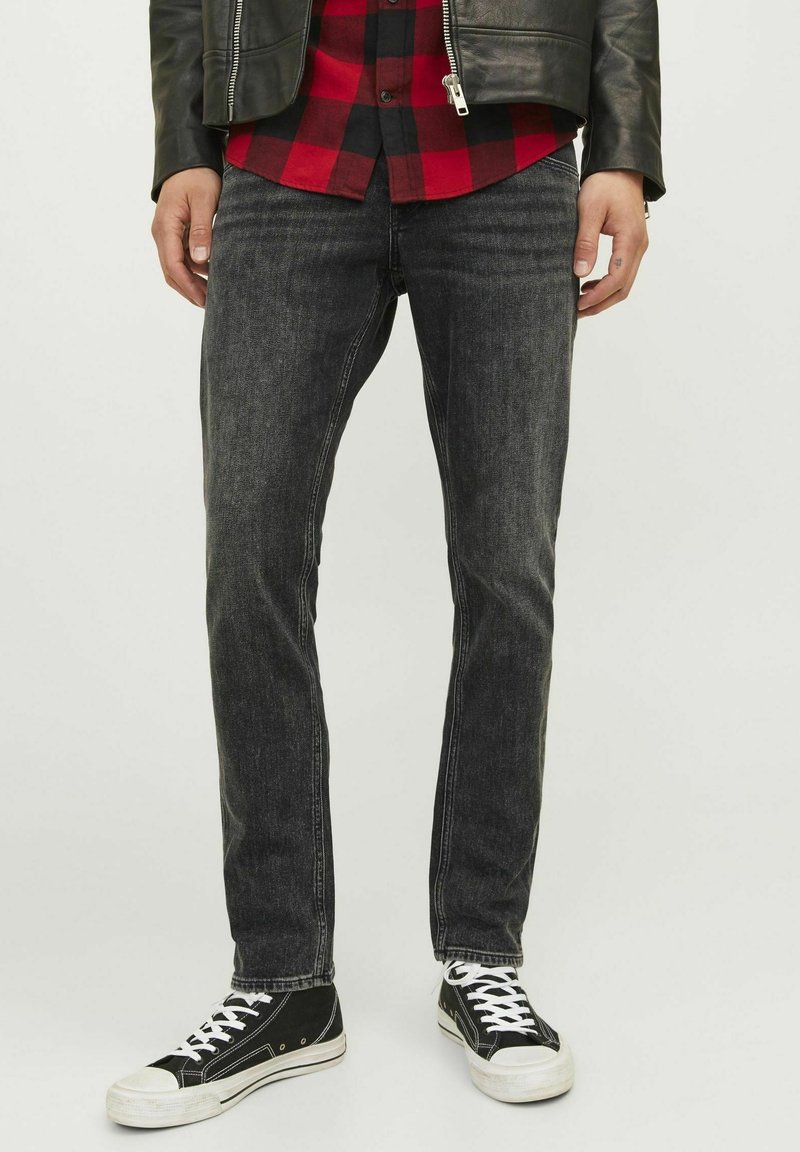 Jeans de denim negro con corte slim, que presentan una textura ligeramente desgastada y un corte recto, combinados con zapatillas altas negras.