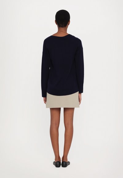 Suéter azul marinho com mangas longas e decote redondo, combinado com uma saia mini bege. Os sapatos são umas sapatilhas pretas. Texturas simples e suaves.