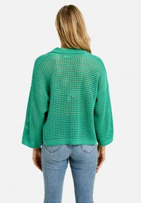 Gr�üner, leichter gestrickter Pullover mit lockerer Passform, der ein atmungsaktives Netzmuster und 3/4-Ärmel aufweist, getragen über engen Jeans.