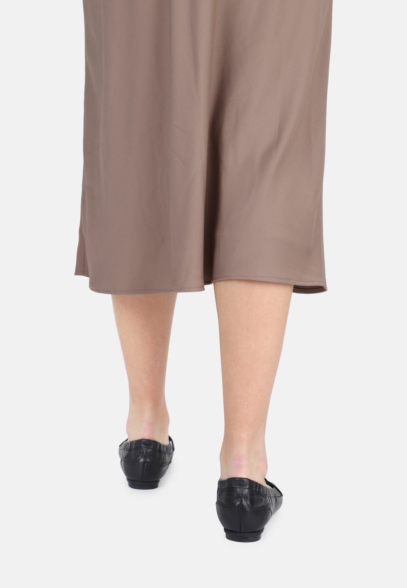 Bruine jurk tot de knie met een gladde textuur, gecombineerd met zwarte, platte leren instappers met een subtiele textuur.