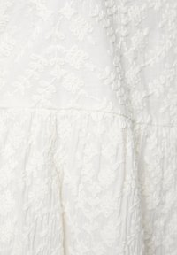 Tissu blanc brodé présentant des motifs de feuilles, surface texturée avec des détails froncés, matériau doux et léger.