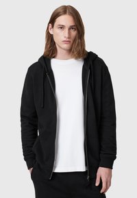 Black zip-up hoodie with a drawstring hood, featuring a smooth texture and side pockets, layered over a plain white t-shirt.