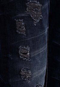 Dunkelblaue Jeans aus Denim mit abgetragenen Stellen und fransigen Kanten, die mehrere eingerissene Bereiche für ein strukturiertes Erscheinungsbild aufweisen.
