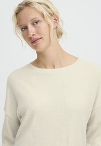 Maglione a coste beige chiaro con scollo rotondo e spalle scese. Tessuto morbido, maniche lunghe e vestibilità rilassata.