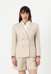 Beige dobbeltradet blazer i linblanding med gullknapper, notched rever og sidelommer, sammen med matchende skreddersydde shorts.