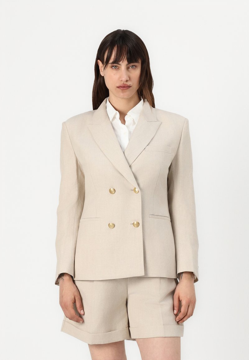 Beige dobbeltradet blazer i linblanding med gullknapper, notched rever og sidelommer, sammen med matchende skreddersydde shorts.