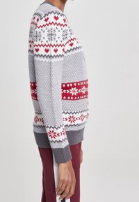 Grauer Strickpullover mit roten und weißen Feiertagsmustern, darunter Herzen, Schneeflocken und geometrische Designs. Lange Ärmel mit gerippten Bündchen.
