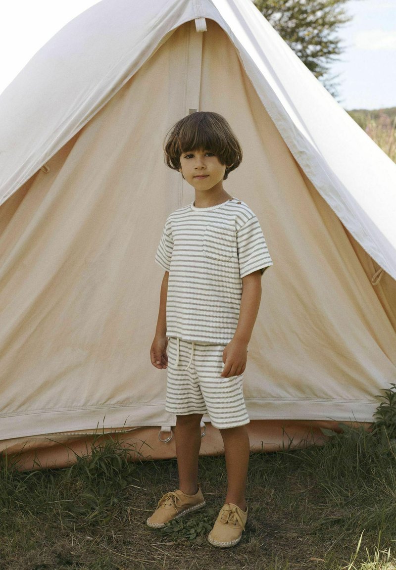 Striped short-sleeve shirt and shorts set in cream and beige. Cotton fabric. Brown shoes. Child stands in front of a beige tent. Grass visible.