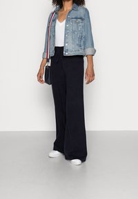 Spijkerjack met een lichtblauwe wassing, cropped ontwerp en opgerolde mouwen, gecombineerd met losse zwarte wijde broek en witte sneakers.